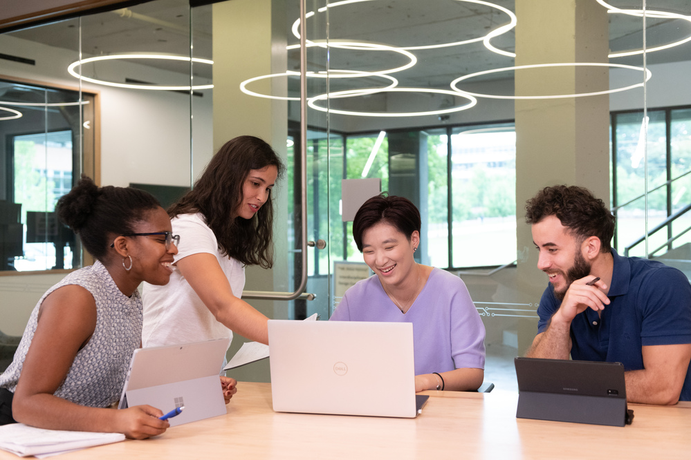 four college students sitting at round table looking at a computer